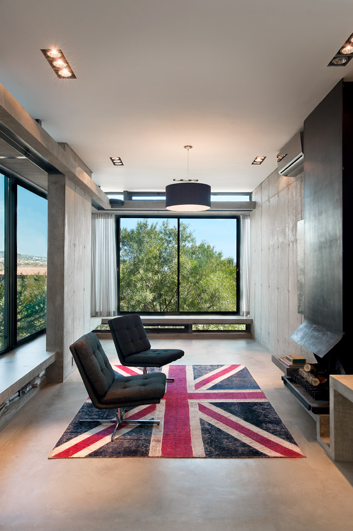 An oversized concrete bay window wraps around the extent of the living room, suspended between glazed infill panels. The smooth lines of the bespoke fireplace are intensified against a backdrop of raw off-shutter concrete and Verde Gauatemala marble. 