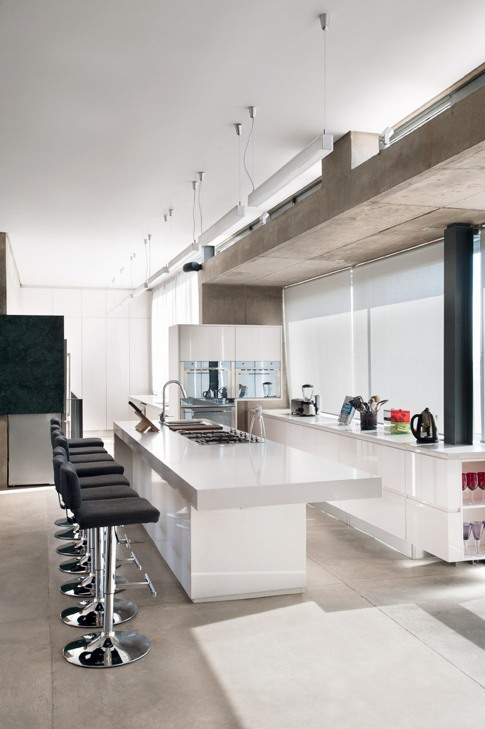 Sunlight spills through the full-height glazing, drenching the open-plan kitchen and living area in natural light. The vertical blinds are translucent, allowing protection against the heat in summer without sacrificing the view. 