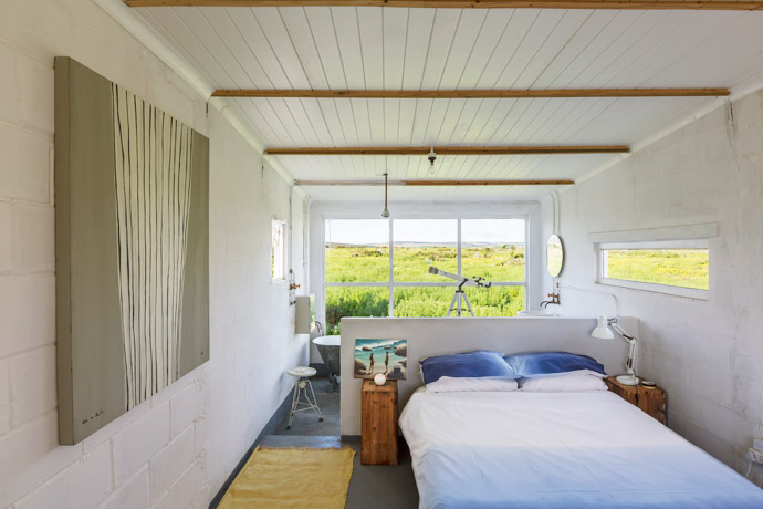 Two wooden paraffin boxes serve as bedside tables. On the one is an oil-on-canvas seascape by artist Louis Nel.