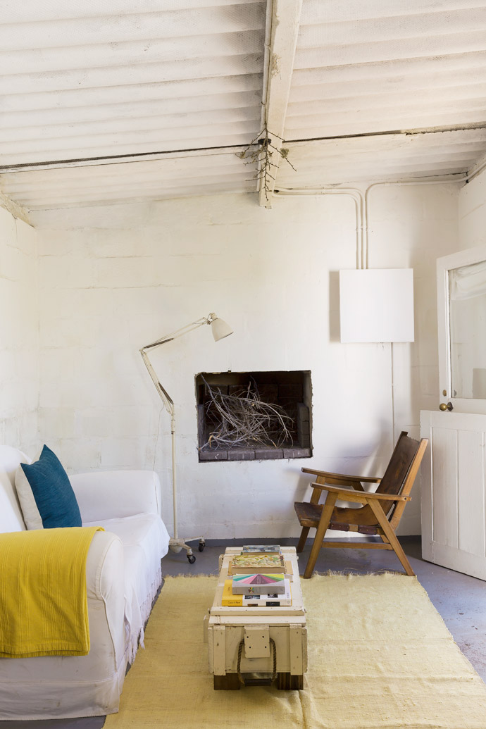 The sparse living space features a 1950s wood-and-leather chair from Mozambique, sat in front of the simple fireplace. 