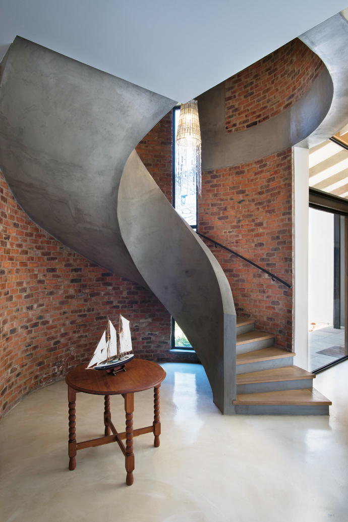 The spiral concrete stairway, French oak flooring and raw brickwork combine to create an earthy anchor to the entrance space.