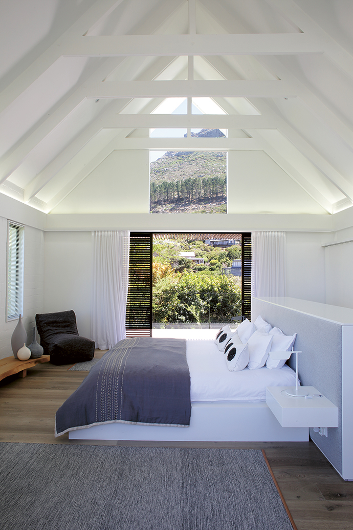 The white exposed beams of the living area are repeated in the master bedroom with its matching triangular window in the eaves that lets the mountain in. The sliding door opens to the garden, pool and entertainment area. Concealed lighting on dimmers allow for warm, soft light. The chairin the corner, sourced in Australia, is a Koskela Quadrant Soft.