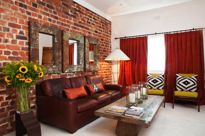 The exposed brick wall hosts recycled antique tin mirrors by Wendy Owen Design in Sonoma, California. The glass candle holders are from Pottery Barn, the iron lamp is by Ron Mann Design, and the chairs are from More Good Stuff. The orange scatter cushions are by The J Factor, the black-and-white ones by Hertex, and the coffee table is an antique mesquite door sourced in Mexico. The silk curtains are by Wendy Owen Design.