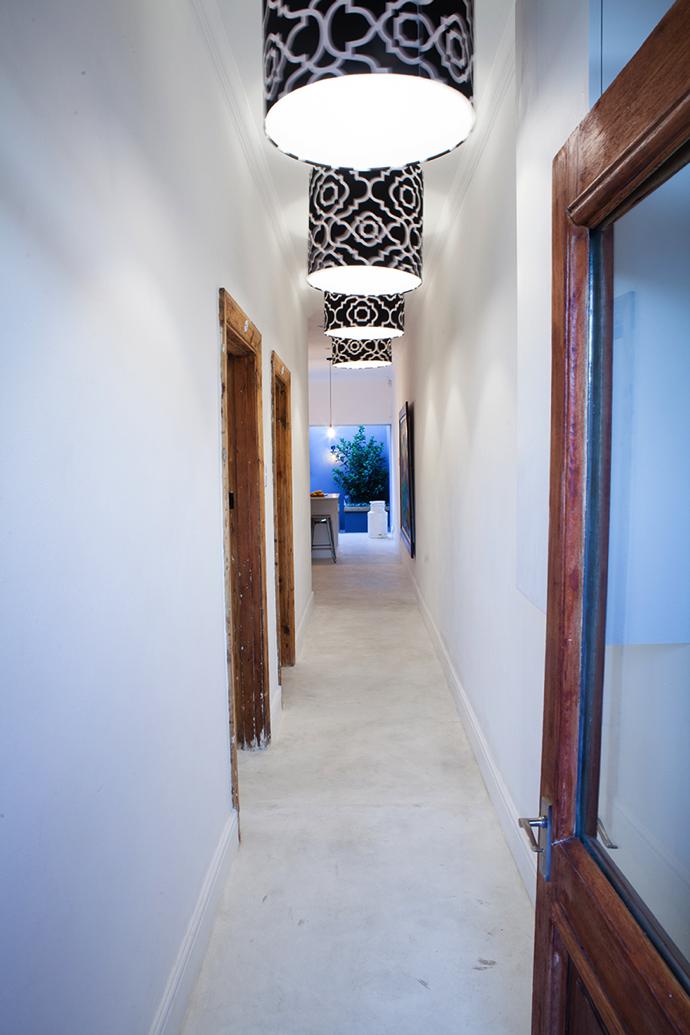 An all-white hallway is lit by custom-made pendant lights with black-and-white shades made by Ivy White Productions with fabric from Constantia Fabrics.