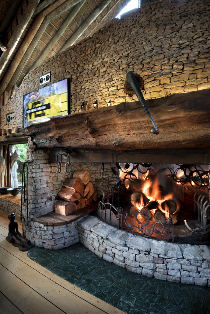 The quirky aesthetic is characterised by unexpected combinations. Here, a modern flatscreen and recessed speakers seem to grow out of an ancient stone wall, and intricate ironwork forms a contrast with the rough-hewn mantelpiece.