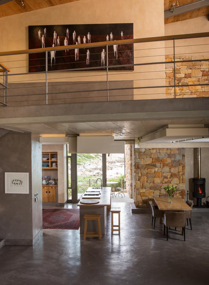 The open-plan living area features stucco fl oors and walls by Stucco Italiano, Table Mountain sandstone cladding by Alexis Mputhi Stone Masons, and a Morsø fi replace. The large painting upstairs is by local artist and gallery owner Victor Harley.
