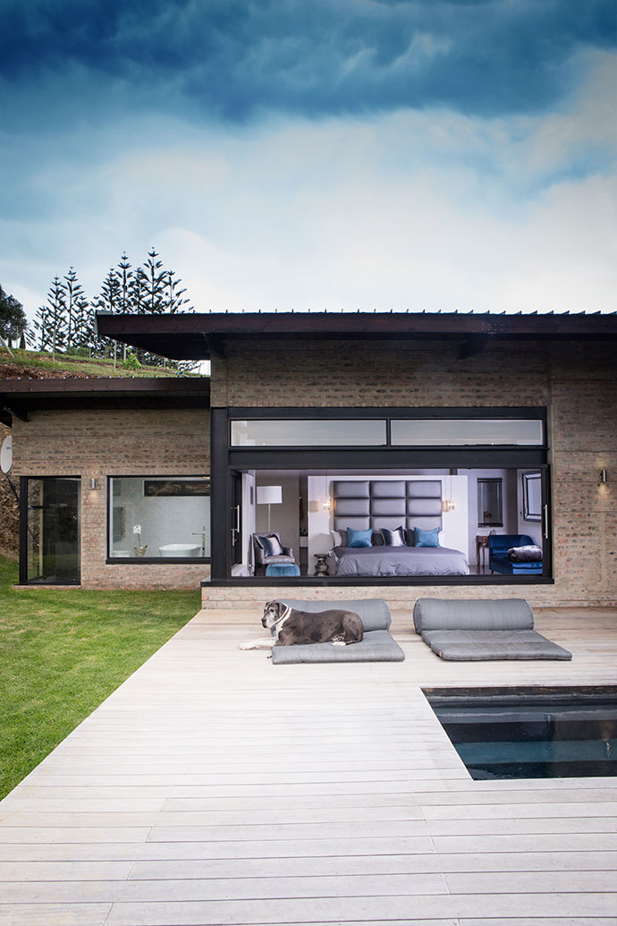 The doors of the main bedroom slide into the walls, opening the entire room to the deck. Fuss-free decor is embellished with plush fabrics, modern bevelled mirrors and a few touches of lustrous metal in bedside pendant lamps and fittings in the en-suite bathroom. One of the Great Danes, Muesli, lolls by the pool.