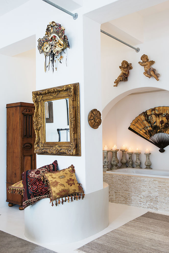 In the bathroom,
candles, Venetian
masks, Italian cherubs, an ornate
gilt mirror, gold
brocade cushions
from Liberty London
and an old Chinese
fan play nicely
with a rustic 1940s
pine cupboard.