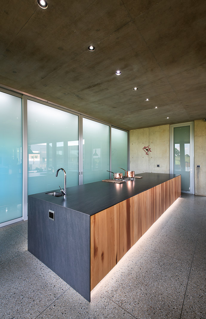 Huge frosted-glass doors conceal the functionalities of daily life such as the fridge and microwave oven. On show is a sleek run of poplar cupboards topped with black Neolith cladding and accessorised with a Hansgrohe tap.
