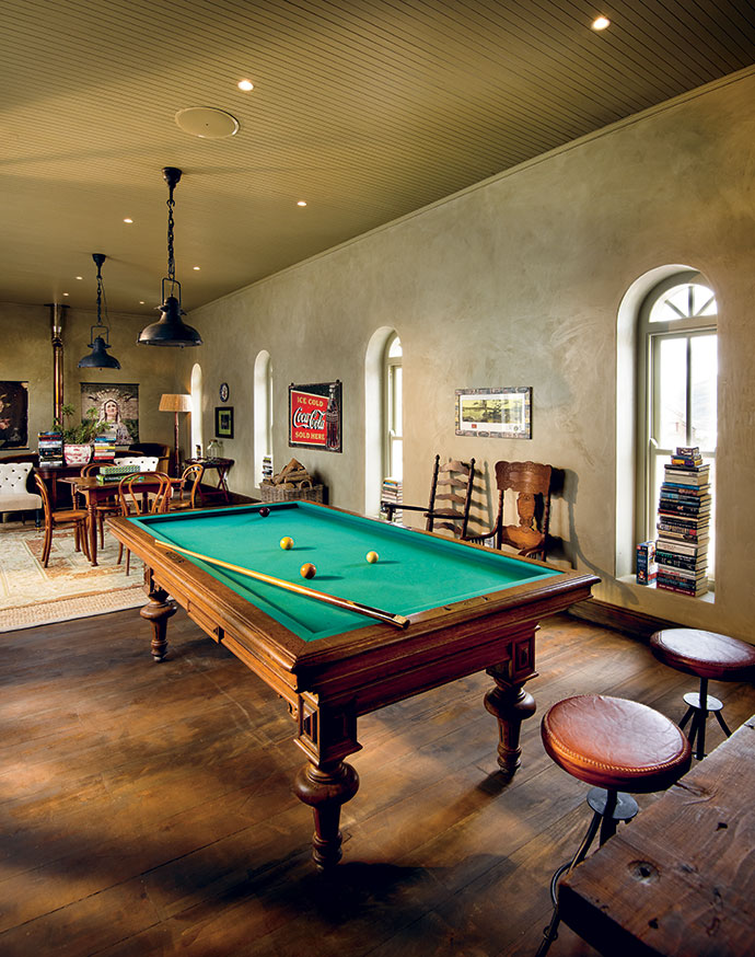 An adult playground, with board games, dartboard, piles of books, comfortable sofas facing a convection fireplace, and an antique French or “carom” billiard table taking centre stage