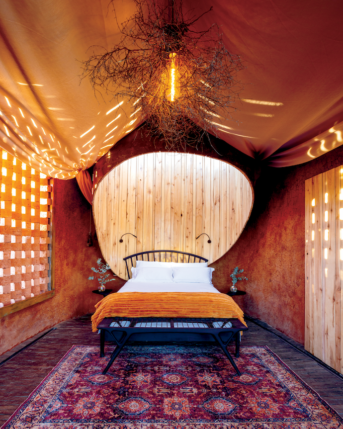 The main bedroom features a headboard/skylight made of yet another piece of the reclaimed metal silo, a window screen of clay bricks by local brickmaker Johnson’s Bricks, a “lampshade” made of dried shrubs picked from the koppie, and an Ella bench with brass riempies by Meyer Von Wielligh.