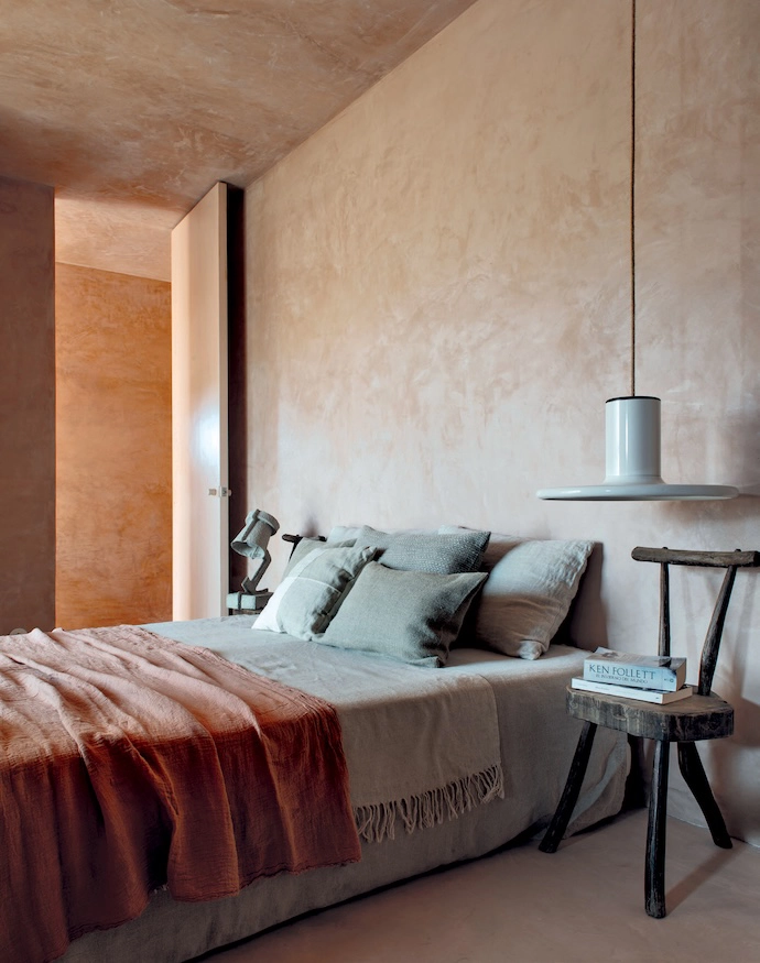 Soft materials in a guest room are accented by a desert-rose throw from Couleur Chanvre, with a wooden chair acting as a bedside table and a Trash Me lamp (made of recycled egg cartons) by New York designer Victor Vetterlein.
