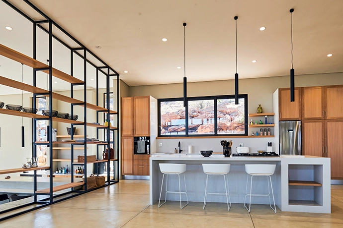 CreteCote flooring by Cemcrete is used to create a cement-based coating that effortlessly unifies kitchen and living areas with its smooth surface. The open shelving and large windows ensure that natural light floods the space.
