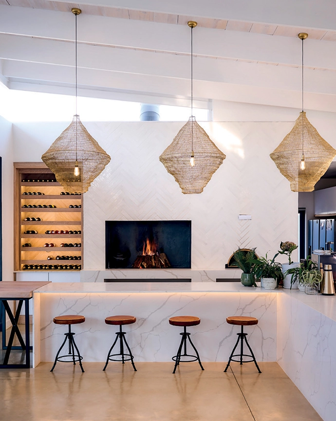 Double-volume ceilings, an expansive L-shaped counter and clever lighting solutions visually connect this space to additional living areas on either side. The CreteCote Dune flooring by Cemcrete is consistent throughout.