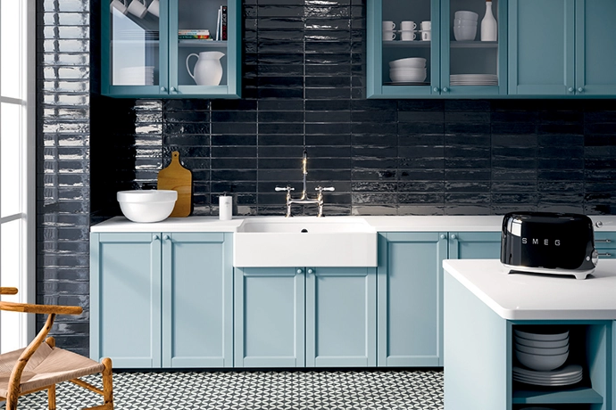 This kitchen layout brims with colour, texture and elegance, courtesy of the porcelain Brianna floor tiles in Enya Coal by Decobella. Smoky-blue cabinetry and a dark, glossy backsplash create a visually striking space. 