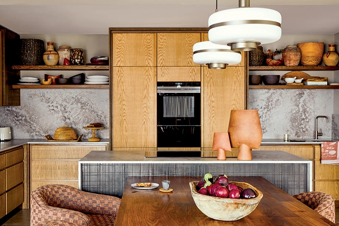 Incorporating curated pieces by La Grange Interiors, the rustic textures in this kitchen add warmth, while the open shelving showcases artisanal ceramics and woven baskets, adding layers of interest.