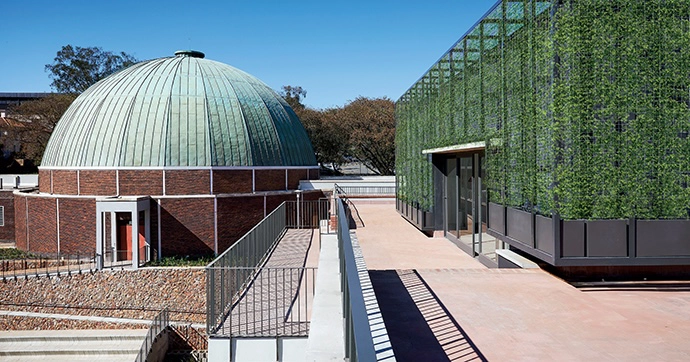 The lift and storerooms on the roof of the extension are covered in a steel mesh box over which creepers will climb, echoing the colour of the copper dome.