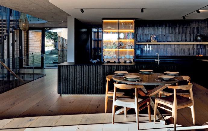 In the kitchen and dining space, an interplay of angles and curves creates a bold architectural statement. The fluted timber island is the work of Timmer Creative Woodwork and JSdesign Consultancy, while the two tall steel-and-glass cabinets were commissioned from The Iron Banister.
