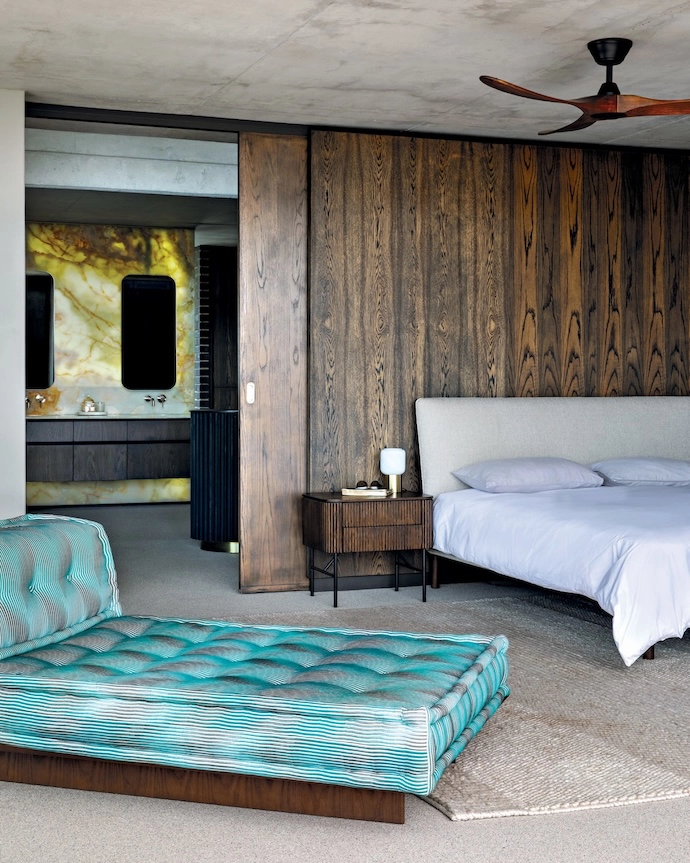 The master bedroom’s wood-panelled walls and sliding door reveal a backlit marble feature, which the owners secured for their bathroom before the house was built.
