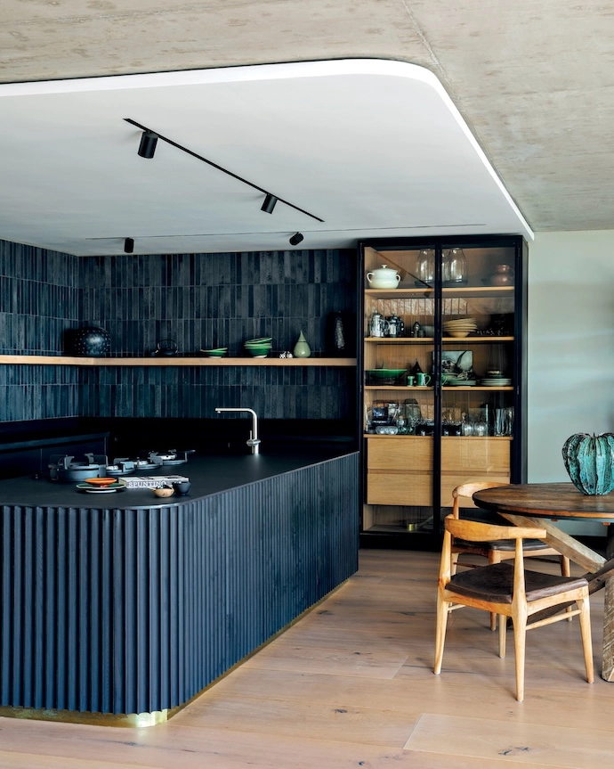 In the kitchen and dining space, an interplay of angles and curves creates a bold architectural statement. The fluted timber island is the work of Timmer Creative Woodwork and JSdesign Consultancy, while the two tall steel-and-glass cabinets were commissioned from The Iron Banister.