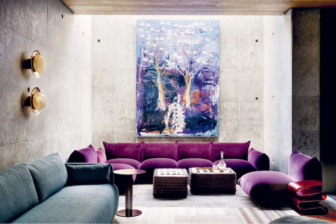 Moody tones and a perfectly lit off-shutter concrete wall in a lounge that leads off the wine cellar and golf simulator in the basement area. The Marenco sofa from Arflex sits beneath an artwork by Beezy Bailey. The wall lights are from Studio 19, the metal sidetable is from Acre Studio and the Perspex sidetable is vintage. The two ottomans were custom-made by Monsoon Interiors for the owners and covered in fabrics by Kirkby Design.