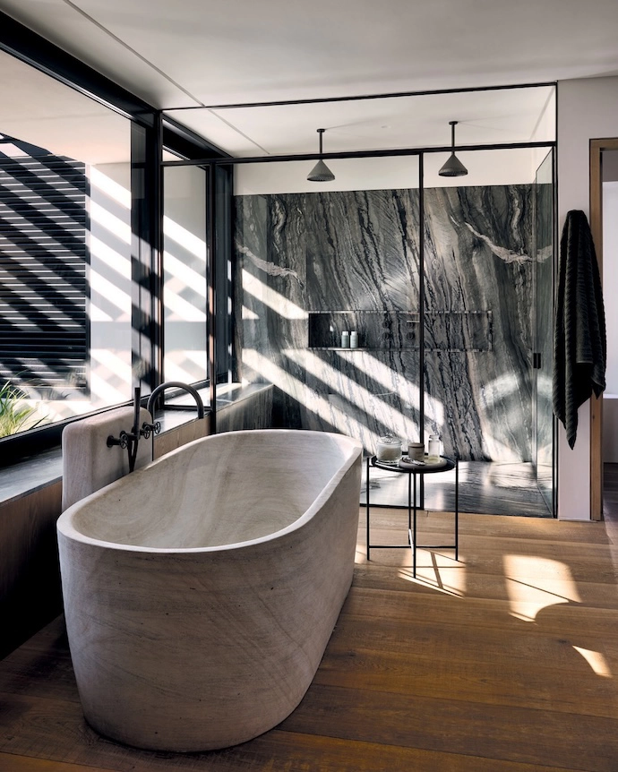 The main bathroom opens onto the same private terrace as the main bedroom. Wooden floors are a warm contrast against the dramatic Afristone slabs in the shower and on the vanity. The stone bathtub is by Bone Studio, and the fixtures are from Lavo Bathroom Concepts.