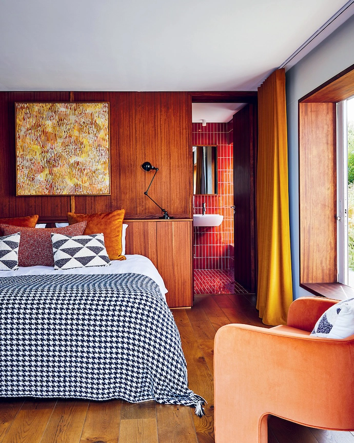 With solid wood floors and wood-panelled walls, the main bedroom is a calming cocoon of autumnal shades and pops of black and white.