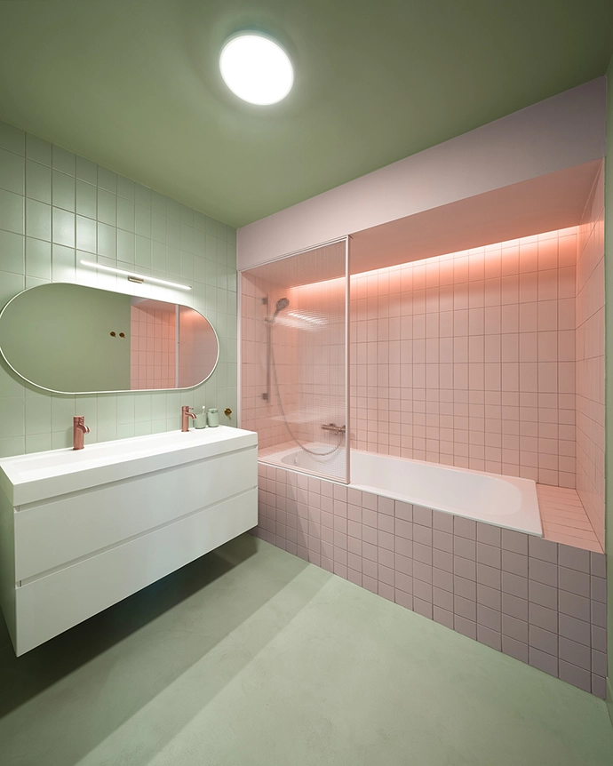 The bathroom combines green with pink ceramic tiles. Subtle copper accents complete the harmony between freshness and elegance.