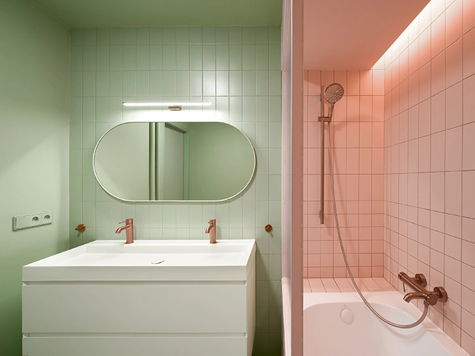 The bathroom combines green with pink ceramic tiles. Subtle copper accents complete the harmony between freshness and elegance.