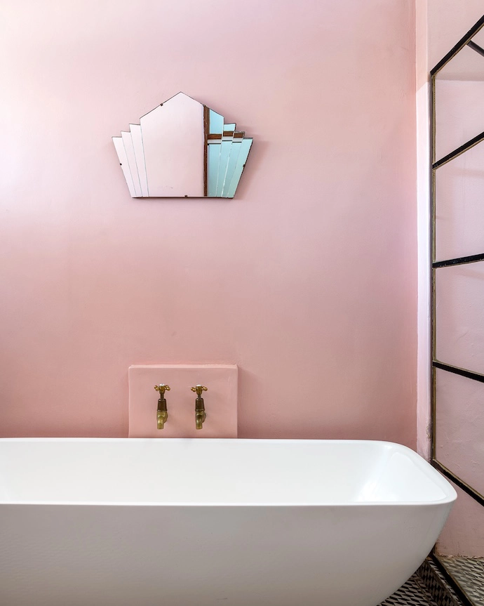 A muted pink wall and delicate Art Deco mirror encourage bath-time contemplation in the contemporary tub.