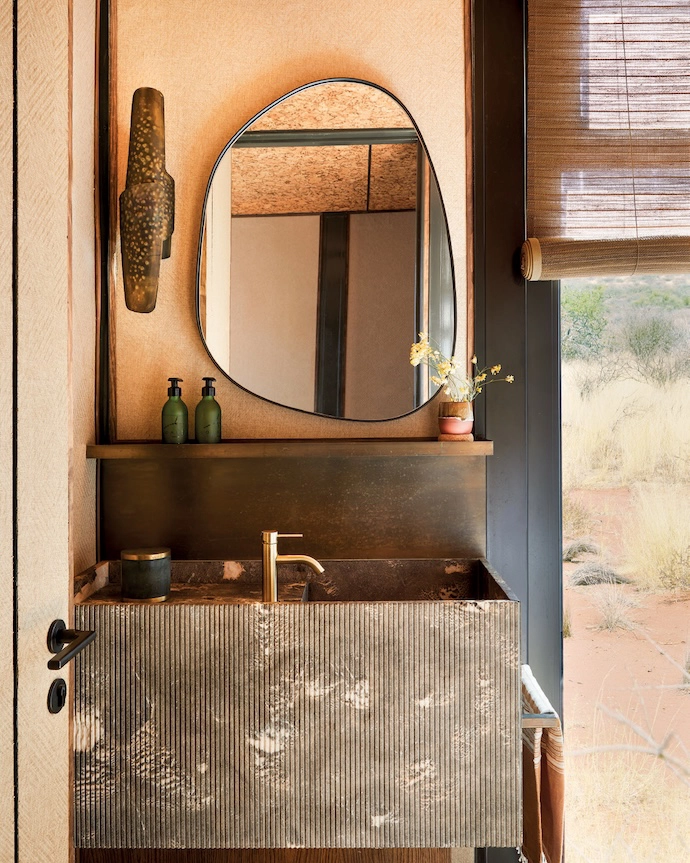 A fluted stone vanity and hammered sconce add the luxe factor to an already textured bathroom by South Africa’s Gregory Mellor Design. Tactile extremes are exaggerated by off setting these surfaces with a woven grasscloth, cork ceiling and bamboo blind.