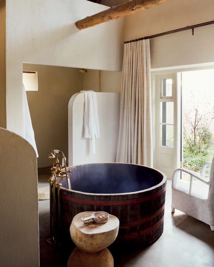 An oversized wooden tub is a statement-making addition to this rustic bathroom by Gregory Mellor Design. Placing it in the centre of the room not only draws attention to its uniqueness, but also connects it with views of the outdoors. The tub is half of a large oak wine barrel, procured by the client on a whim. It had to be sanded very smooth to remove all splinters, and then thoroughly sealed with a waterproof product. Unlacquered brass tapware elevates the look.