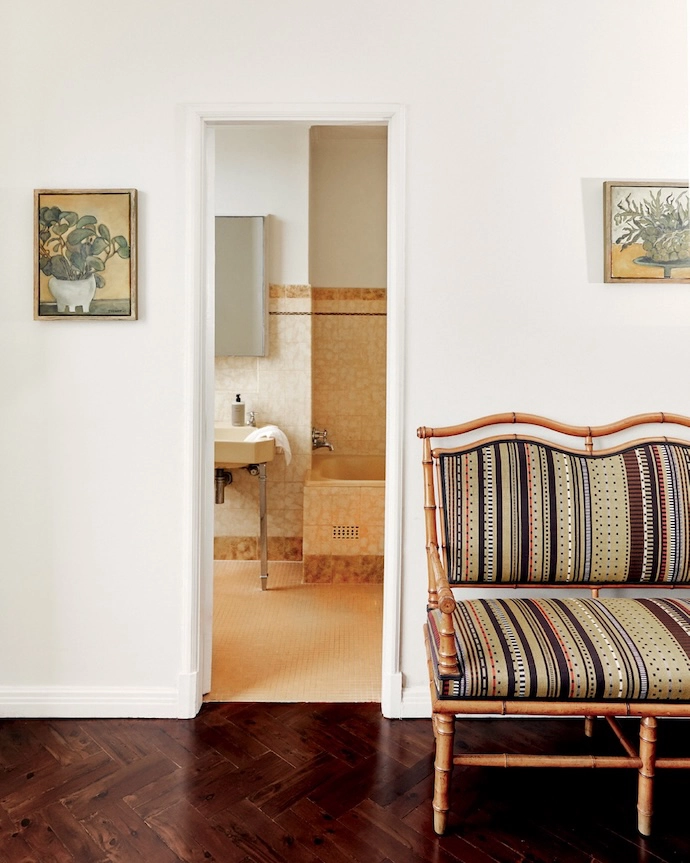Artworks by the owner and a 19th-century French carved wooden bench reupholstered in a Paul Smith fabric flank the door to the main bathroom.