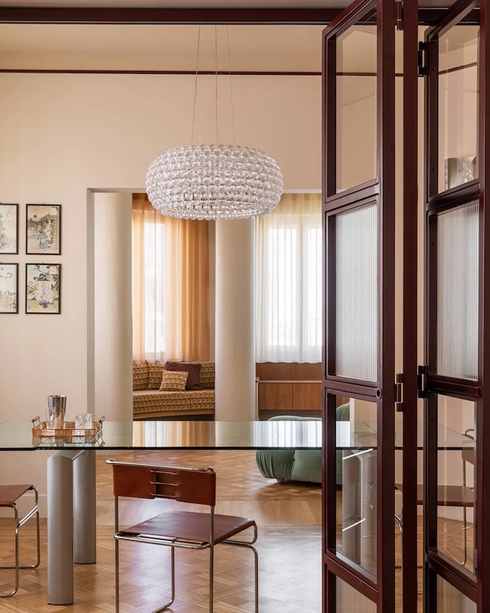 View of the dining room from the reading area featuring Libellula chairs, designed by Giovanni Carini for Planula; Caboche Plus Grande pendant lamp by Foscarini; Camaleonda sofas, designed by Mario Bellini for B&B Italia; custom bench in Relief Cammello fabric by l’Opificio, and curtains in FISCHBACHER fabric 113/117/132. 