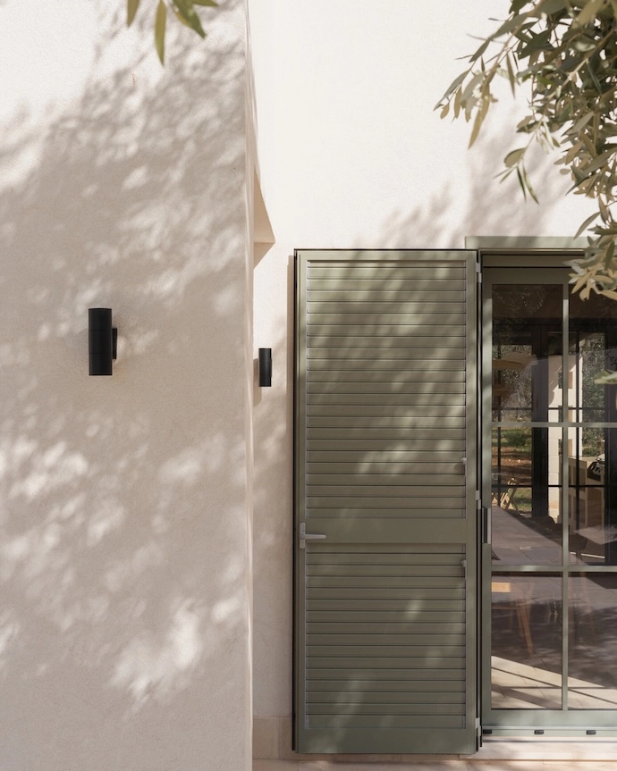 Large folding windows orient both villas toward the pool and olive grove, dissolving the threshold between inside and out.