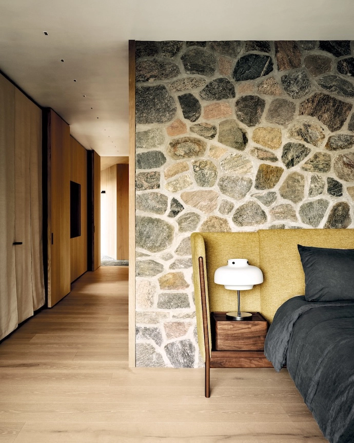 The primary bedroom boasts a fieldstone wall and cupboards (with suspended rugs for doors to soft en the space). The lamp is by &Tradition.
