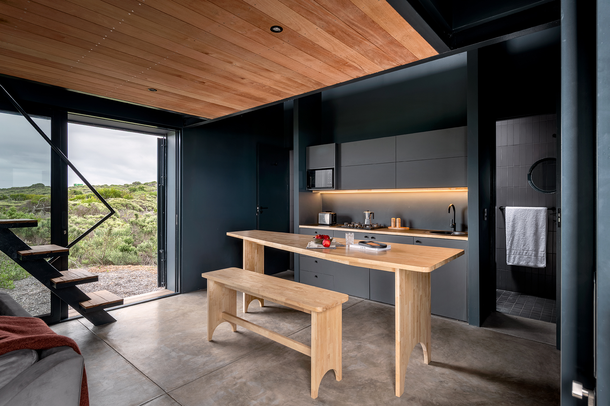 A study in masculine greys, the pared-down open-plan kitchen/dining space features sliding doors that encourage alfresco entertaining. A shower room is tucked behind the wall of the work area.