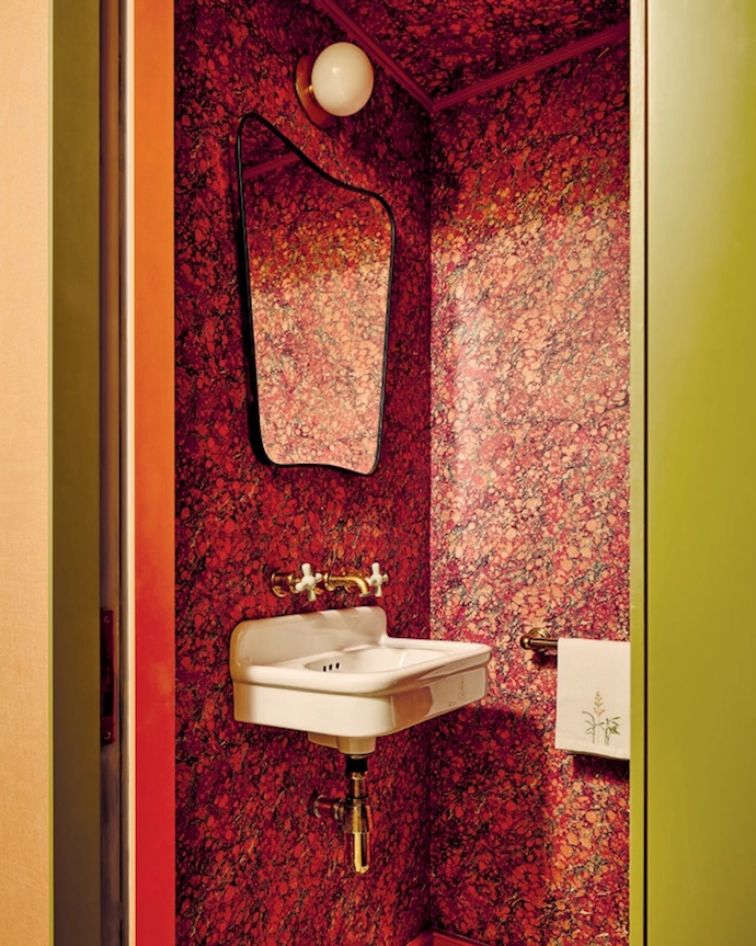 At Palace Gardens residential project in Notting Hill, London, warm terracotta hues and sage-green contrasts dominate the palette – in the entryway, the lounge anchored by a curved sofa, the dining area with its textured wallpaper, and the deep-red marbled wallpaper that’s been used in the guest bathroom. The kitchen continues the earthy aesthetic with luxe stone surfaces.