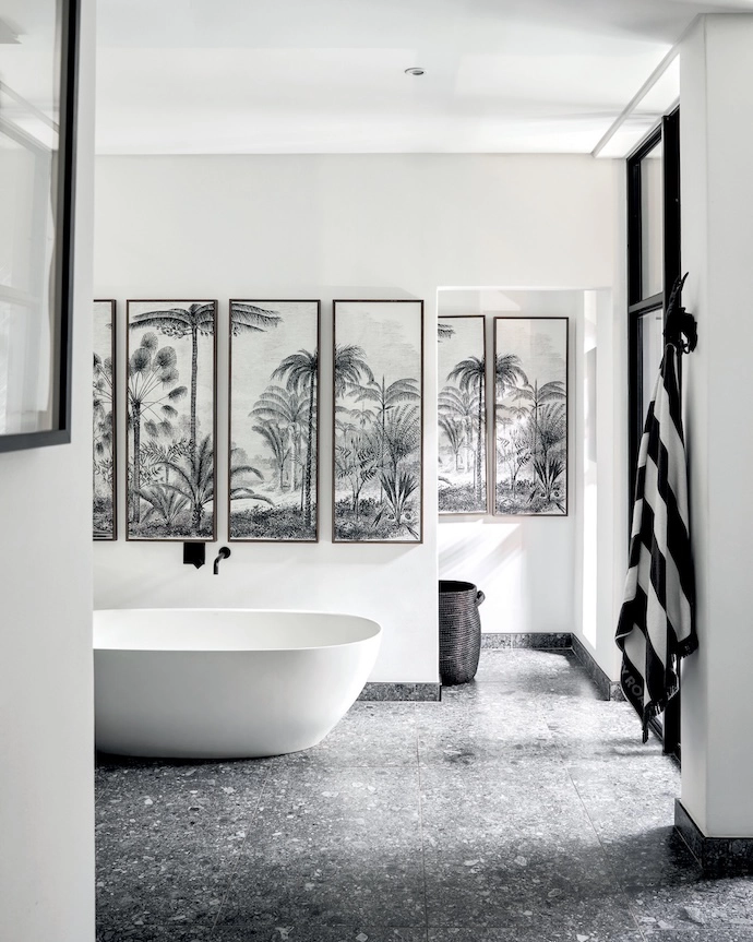 Terrazzo flooring adds texture in the main bathroom, which is a study in monochrome tones. The bathtub is by Livingstone Baths, the tapware is from Gio Plumbing, and the vanity unit was custom-designed by Erica. The multi-frame art pieces above the tub and in the adjacent WC are thrift-shop finds.