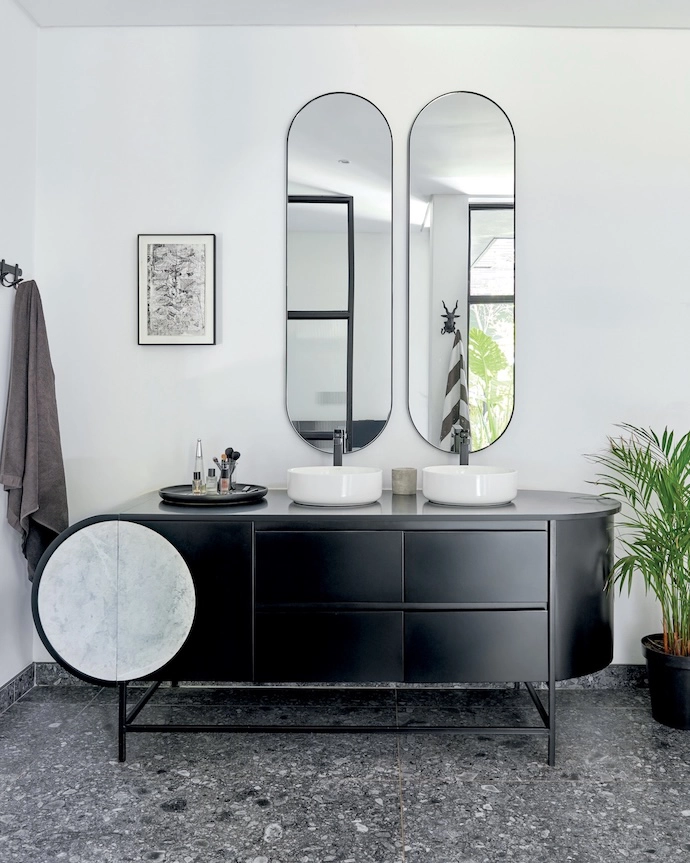 Terrazzo flooring adds texture in the main bathroom, which is a study in monochrome tones. The bathtub is by Livingstone Baths, the tapware is from Gio Plumbing, and the vanity unit was custom-designed by Erica. The multi-frame art pieces above the tub and in the adjacent WC are thrift-shop finds.