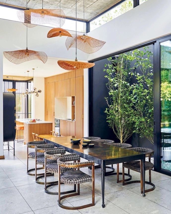 A planted courtyard next to the dining area allows morning light into the space. The dining table is by James Mudge, the chairs by Egg Designs are upholstered in a fabric by Hertex, and the woven lampshades are from Weylandts.