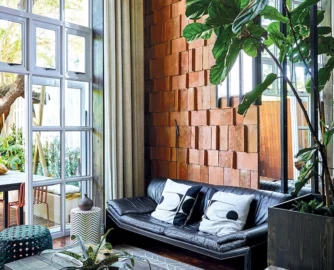 The terracotta roof tiles on the wall catch light across their uneven surfaces, giving the tall room a warmth that paint or plaster can’t match.