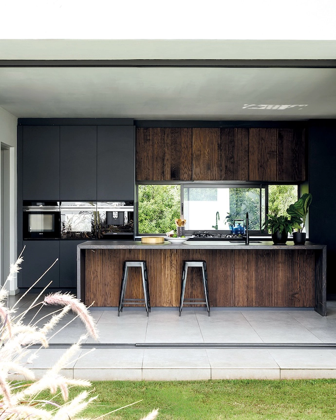The open-plan kitchen’s natural timber and charcoal finishes offer a dramatic counterbalance to the white of the building.