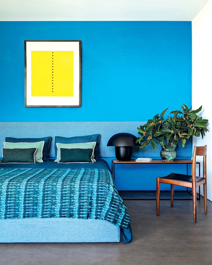 In one of the bedrooms, blue unfolds from the headboard to the walls and the linen by La Redoute Intérieurs. The artwork is a lithograph by Lucio Fontana.