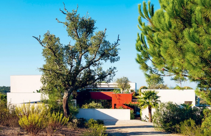 Surrounded by almost-untouched nature, the home sets its contemporary volumes – tinged in red and white – in dialogue with the lush vegetation. Palm trees, agaves, olive trees and climbing vines frame and crown the building.