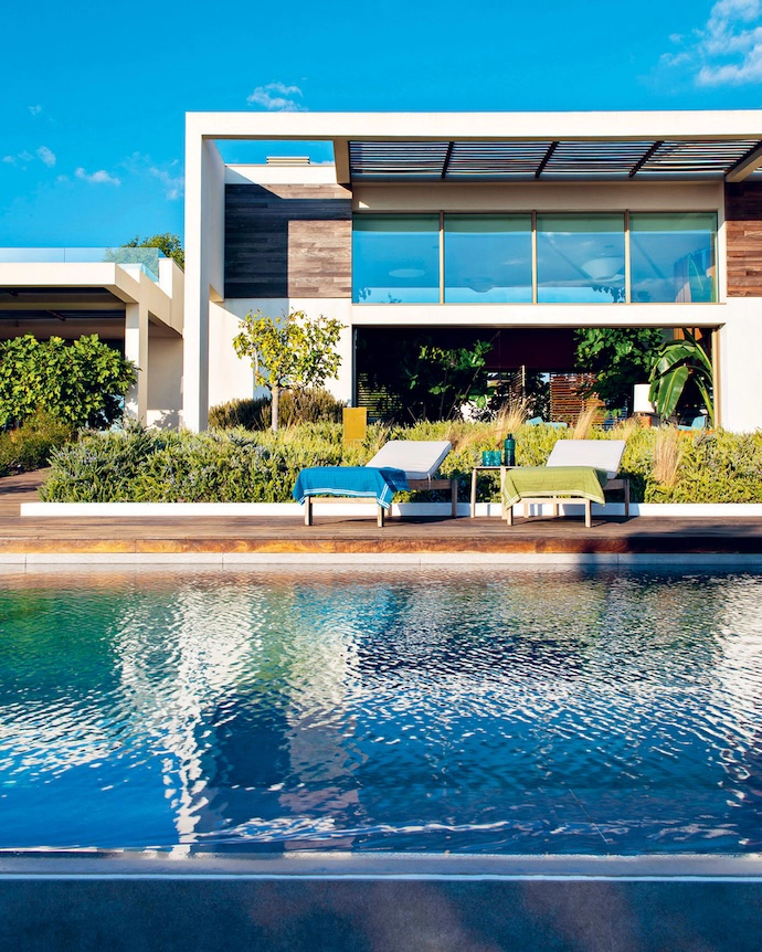 Surrounded by almost-untouched nature, the home sets its contemporary volumes – tinged in red and white – in dialogue with the lush vegetation. Palm trees, agaves, olive trees and climbing vines frame and crown the building.