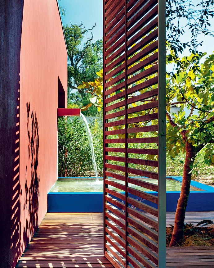 The patio and its water feature reveal themselves through large pivoting panels of slatted wood, extending the living space to the outdoors.