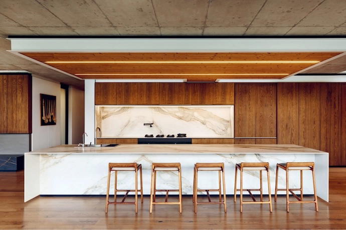 The kitchen occupies a section of the open-plan living area, and is central to large family gatherings. Timber and natural stone finishes add warmth and texture.