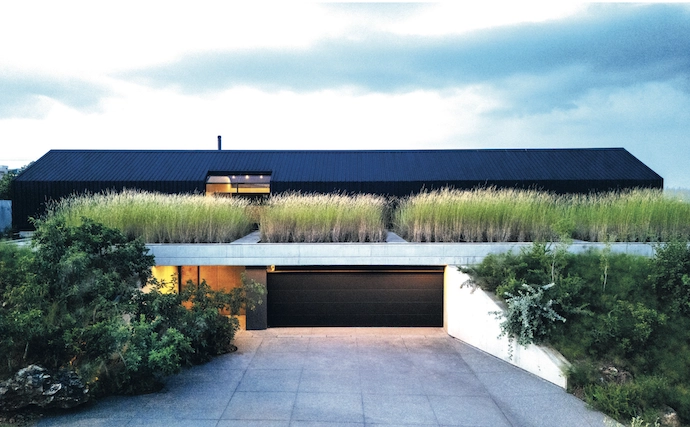 From the street, the house is reduced to a simple shed-like structure floating above a field of grass.