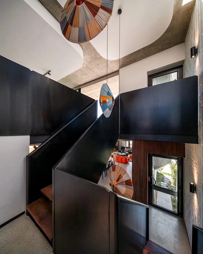 A steel staircase in the triple-volume central well forms the heart of the interior around which other spaces are arranged. Pendant lights by Ashanti Design are suspended for dramatic effect.